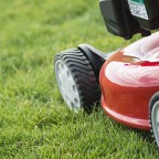 A young man mowing the grass on a property, tending the garden, using a petrol lawnmower.