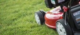A young man mowing the grass on a property, tending the garden, using a petrol lawnmower.